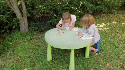 Two sisters drawing with fineliners in notebooks at a small table in a summ.. Stock Footage 304149102