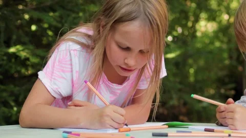Two sisters drawing with fineliners in notebooks at a small table in a summ.. Stock Footage 304149106