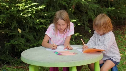 Two sisters drawing with fineliners in notebooks at a small table in a summ.. Stock Footage 304149183