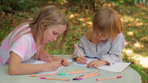Two sisters drawing with fineliners in notebooks at a small table in a summ.. Stock Footage 304149185