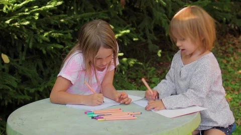 Two sisters drawing with fineliners in notebooks at a small table in a summ.. Stock Footage 304149187
