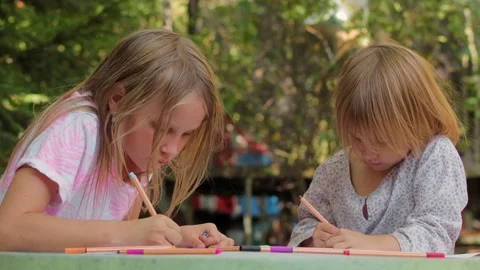 Two sisters drawing with fineliners in notebooks at a small table in a summ.. Stock Footage 304149188