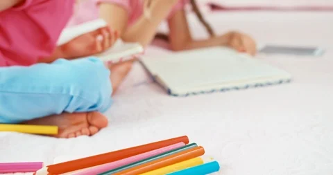 Two sisters drawing in their notebooks, girls are on the bed Stock Footage 95647821