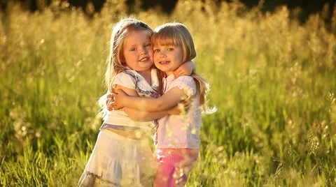 Two sisters embrace. Look at camera. They play in the meadow. Stock Footage