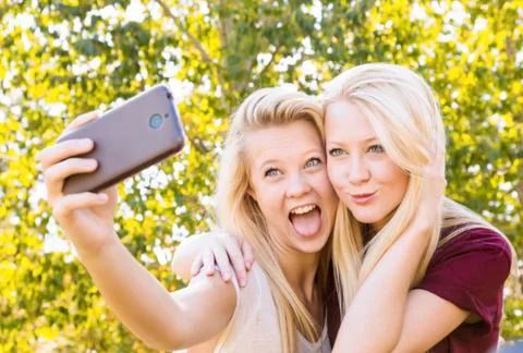 Two sisters having fun outdoors in a city park in autumn and taking selfies of t Foto stock