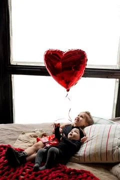 Two sisters hold a heart-shaped balloon in their hand. Stock Photos