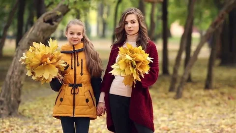 Two sisters holding hands while walking in the autumn park Stock Footage 69167442