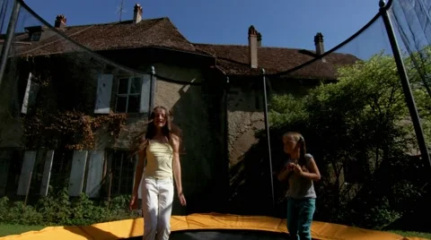 Two sisters, jumping on a trampoline in the courtyard of a village house Stock Footage 60030695