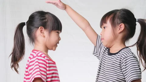 Two sisters measuring height together on white background in studio.  Video stock 171315757