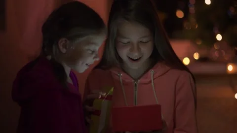 Two sisters open a christmas gift near the christmas tree, light from the gift b Vídeo Stock 145020707