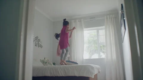 Two sisters playing in the their room and jumping on the bed Stock Footage 279730513