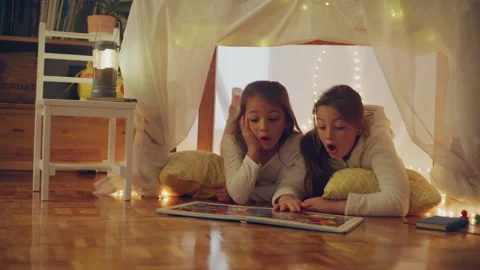 Two sisters playing under the blanket fort at home and reading something Stock Footage 279744701