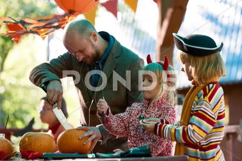 Two sisters playing while their father carving pumpkin Stock Photos