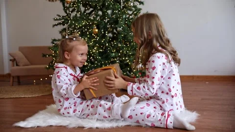 Two sisters pulling big wrapped gift box, fighting near decorated Christmas tree Stock Footage 295417399
