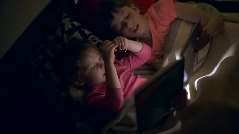 Two sisters reading a book with a flashlight in a dark room at night Stock Footage 103312875