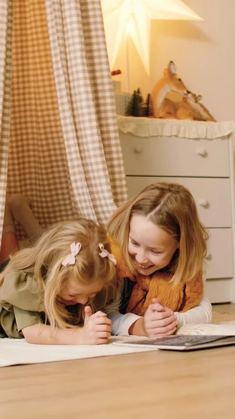 Two sisters reading a book lying in a kinds' play tent at Christmas time. Stock Footage 293288057