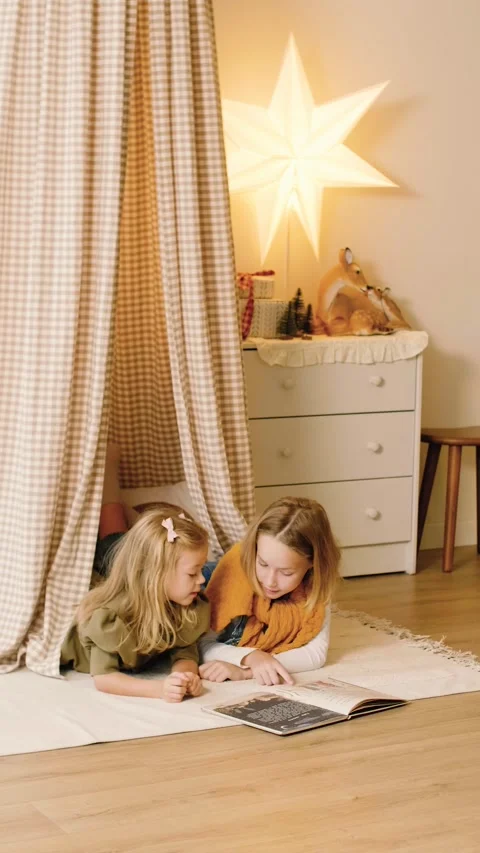 Two sisters reading a book lying in a kinds' play tent at Christmas time. Stock Footage 293288075