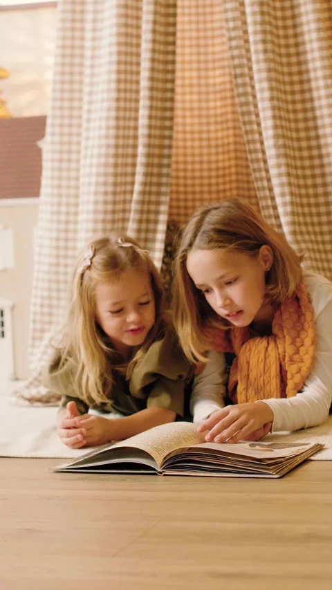 Two sisters reading a book lying in a kinds' play tent at Christmas time. Stock Footage 293288245