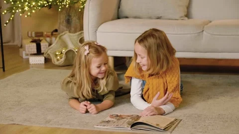 Two sisters reading a book lying on a rug at Christmas time. Stock Footage 293288703