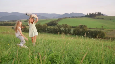 Two sisters running by high green grass meadow with pillows while they have outd Video stock 250273461