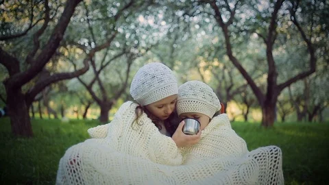 Two sisters sheltered by a plaid sitting in the park Видео 91288431