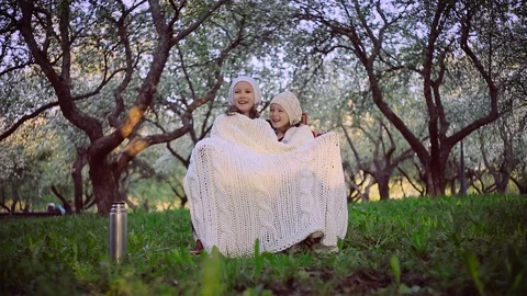 Two sisters sheltered by a plaid sitting in the park Stock Footage 94496503