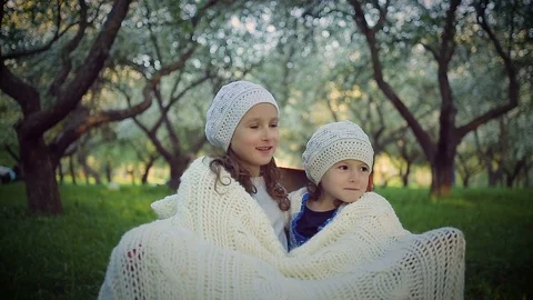 Two sisters sheltered by a plaid sitting in the park Stock Footage 94496939