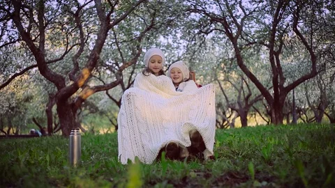Two sisters sheltered by a plaid sitting in the park Stock Footage 100165252