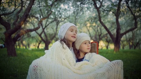 Two sisters sheltered by a plaid sitting in the park Stock Footage 100165564