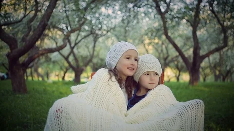 Two sisters sheltered by a plaid sitting in the park Stock Footage 100166058