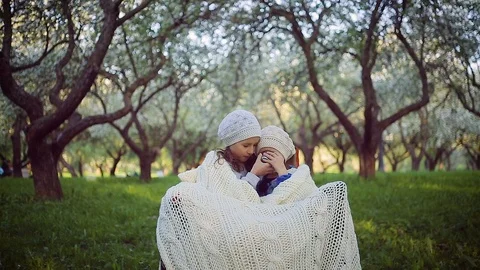 Two sisters sheltered by a plaid sitting in the park Stock Footage 106439943