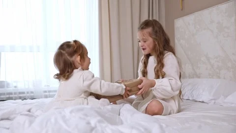 Two sisters sit on a bed, pull big wrapped gift box, fighting, cannot share gift Stock Footage 314063005