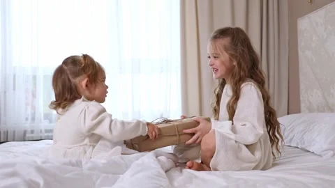 Two sisters sit on a bed, pull big wrapped gift box, fighting, cannot share gift Stock Footage 314063008