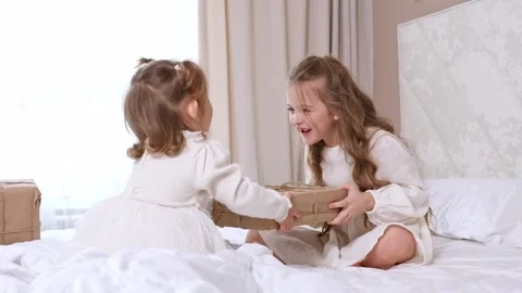 Two sisters sit on a bed, pull big wrapped gift box, fighting, cannot share gift Stock Footage 314063017