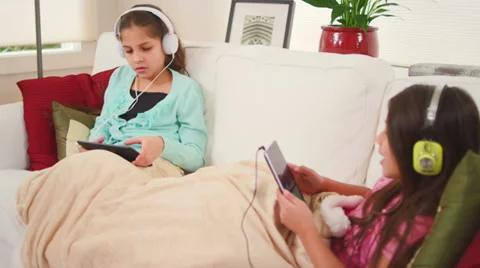 Two sisters sit on a couch and independently sing along to their own music Stock Footage 34015183