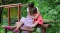Two sisters sits on a wooden log at a sports ground and embraces HD Footage