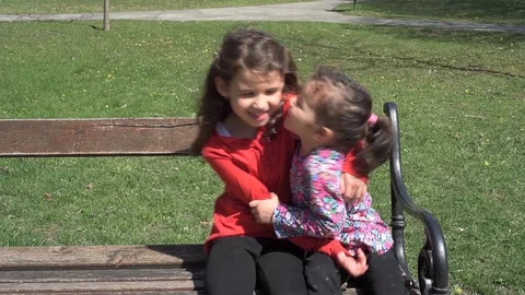 Two sisters sitting and playing on the bench in the city park Stock Footage 88338397