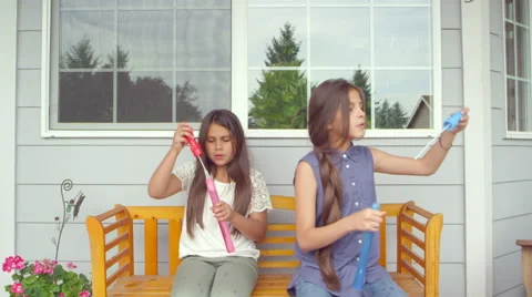 Two sisters sitting on a bench on their porch stand up and start making bubbles Video stock 47787288