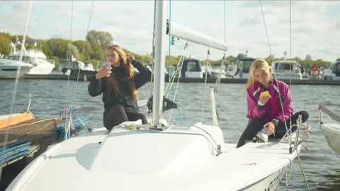 Two sisters sitting on board a white sports yacht take selfies on smartphones Stock Footage 145525781