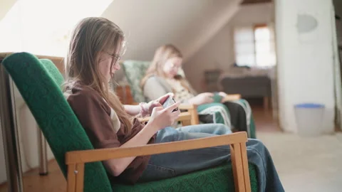 Two sisters sitting in comfortable chair in kids' room cheerfully smiling and la 動画素材 325267659