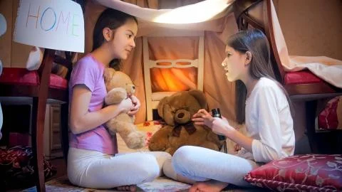 Two sisters sitting in selfmade tepee tent in bedroom and telling scary stories Stock Photos