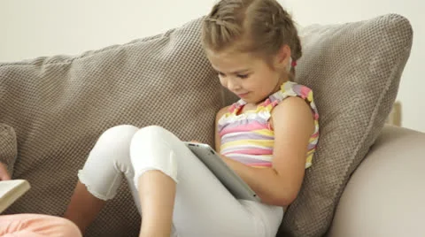 Two sisters sitting on sofa with book and tablet pc Stock Footage 24568197