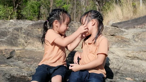 Two sisters smile at each other as they play together on the rocks by the stream Stock Footage 171210053
