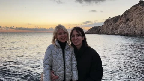 Two sisters smiling at sunset by the sea Stock Footage 303426678