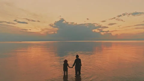 Two sisters standing knee deep in the sea looking at the beautiful sunset Stock Footage 191618312