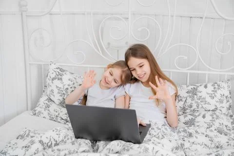 Two sisters study on computer online at home bed. Foto stock