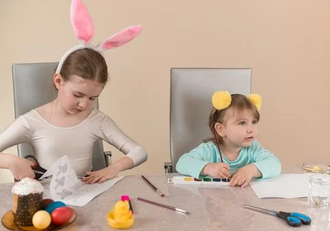 Two sisters at the table draw with paints and cut out paper crafts for Easter Stock Photos