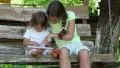 Two sisters with tablet PC sits on the swing bench HD Footage