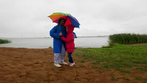 Two Sisters Under Rainbow Umbrella by Lakeside in Rain Stock Footage 297700905