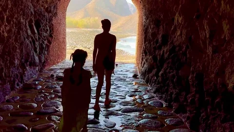 Two sisters walk through a tunnel to a beach with beautiful views. Stock Footage 308002999